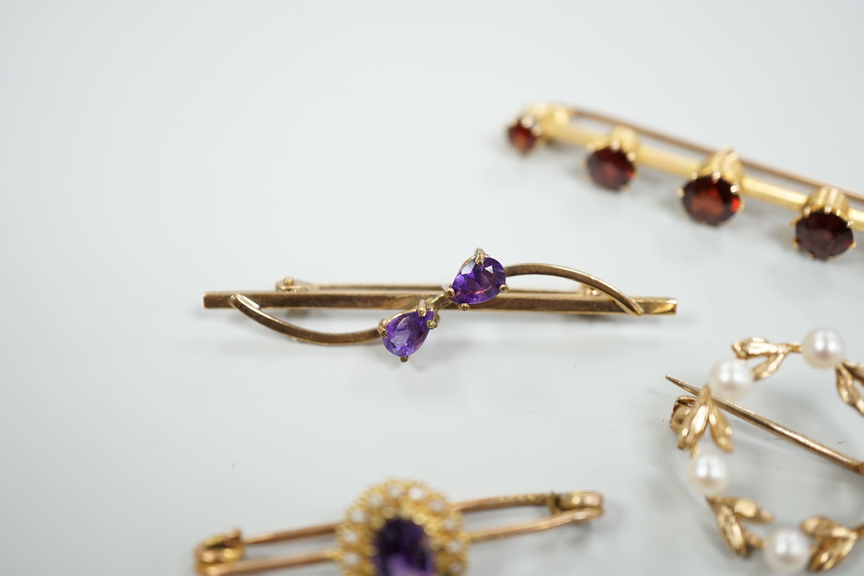 A 15ct and graduated five stone garnet set bar brooch, 48mm, a similar amethyst and seed pearl cluster set brooch and two other gem set brooches, including 9ct gold.